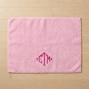 May include: A rectangular light pink bath towel featuring a dark pink embroidered monogram in the center. The monogram consists of the letters E, T, and M arranged in a diamond shape with a decorative border.