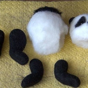 Puede incluir: Un conjunto de piezas de panda de fieltro para manualidades, que incluye la cabeza, el cuerpo y cuatro patas. La cabeza es blanca con orejas y ojos negros, y el cuerpo es blanco. Las patas son negras.