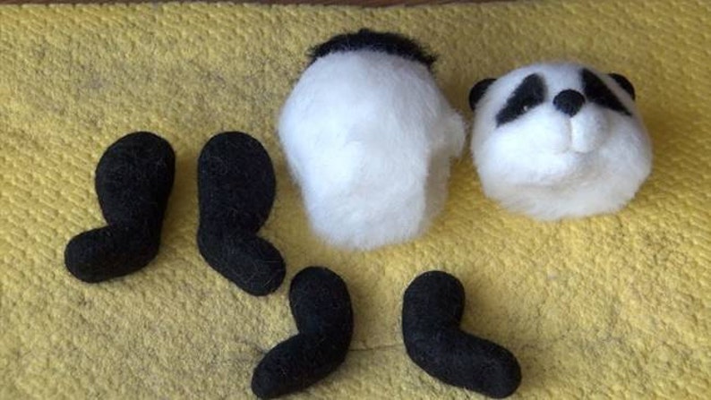 Puede incluir: Un conjunto de piezas de panda de fieltro para manualidades, que incluye la cabeza, el cuerpo y cuatro patas. La cabeza es blanca con orejas y ojos negros, y el cuerpo es blanco. Las patas son negras.