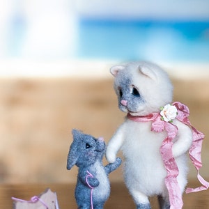 May include: A white and gray cat with blue eyes and a pink ribbon is standing next to a gray mouse with a pink string. The mouse is pulling a wooden toy horse.