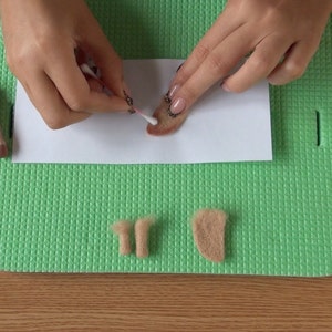 Puede incluir: Una persona utiliza un bastoncillo de algod&oacute;n para difuminar fieltro marr&oacute;n sobre un papel blanco. Hay dos piezas peque&ntilde;as de fieltro marr&oacute;n y una pieza de fieltro marr&oacute;n m&aacute;s grande sobre una alfombra verde.