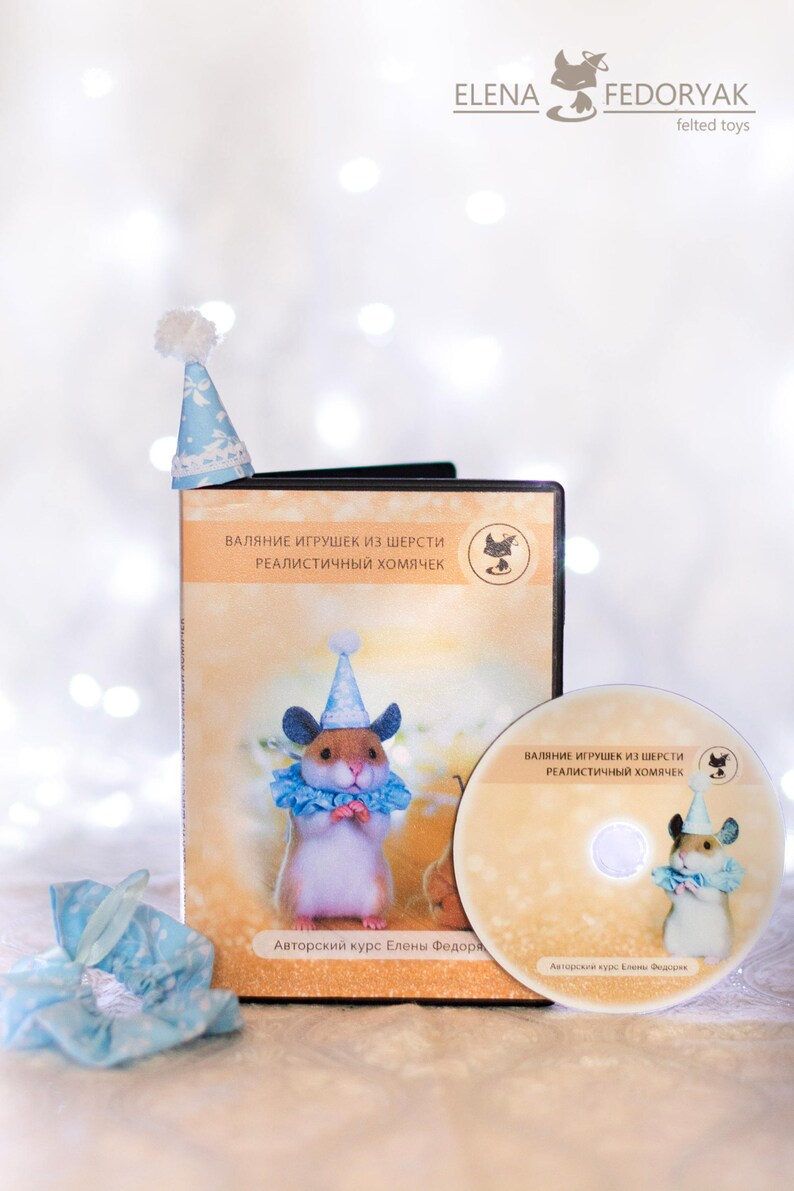 May include: A DVD case and disc featuring a felt hamster wearing a blue and white party hat. The case and disc have the text "Валяние игрушек из шерсти Реалистичный хомячек" and "Авторский курс Елены Федори" on them.