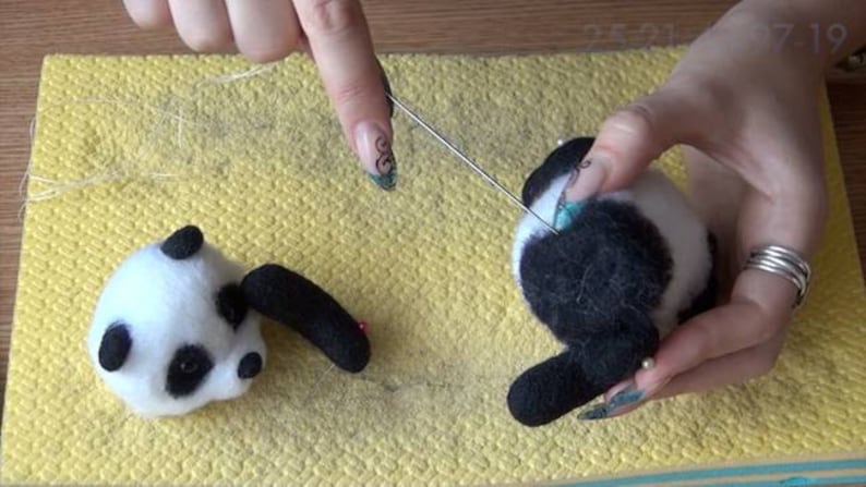 Puede incluir: Una persona est&aacute; haciendo fieltro con aguja un oso panda blanco y negro. El panda se est&aacute; haciendo fieltro en una alfombra amarilla. La persona est&aacute; usando una herramienta de fieltro con aguja para dar forma al pelaje del panda.