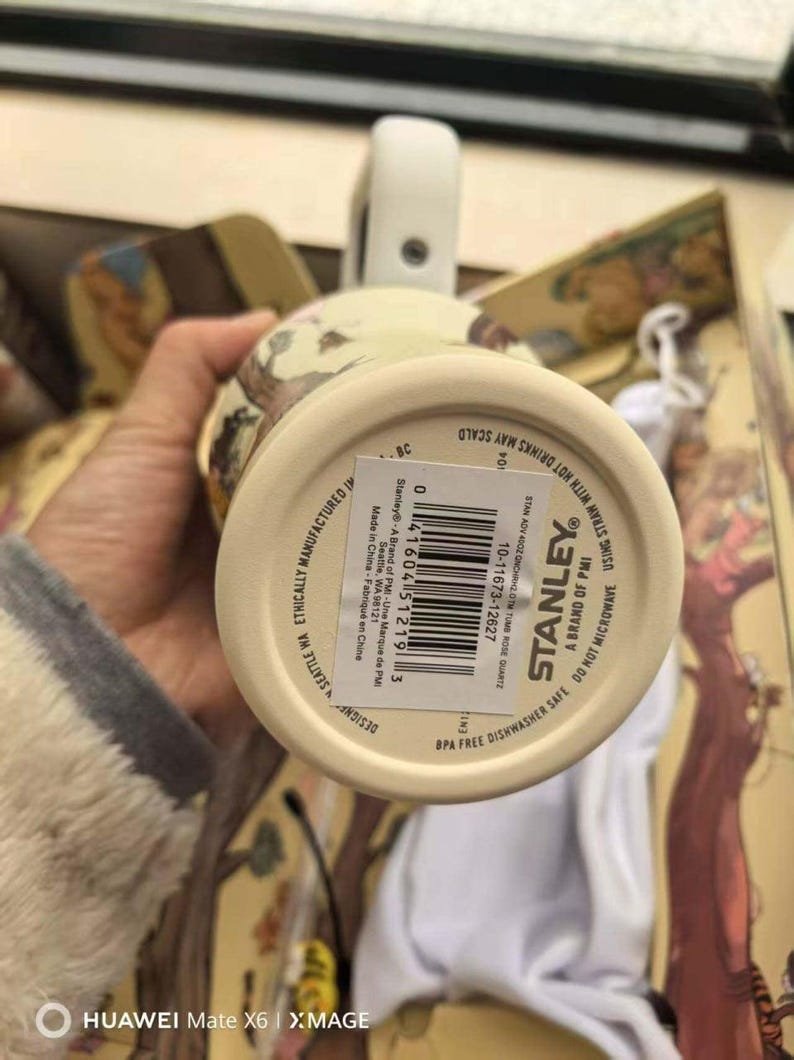 May include: A cream-colored Stanley mug with a white handle and a floral design. The bottom of the mug has a label with the Stanley logo and product information. The mug is BPA-free and dishwasher safe.