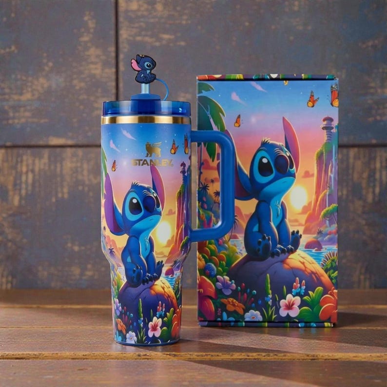 May include: A blue Stanley tumbler with a handle and a straw topper featuring the character Stitch. The tumbler displays a colourful tropical sunset scene with Stitch sitting on a rock surrounded by flowers. The matching box shows the same graphic.
