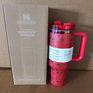 May include: A red Stanley Quencher H2.0 FlowState tumbler with a repeating metallic logo pattern, a red handle, and a red lid, standing next to its cardboard packaging box which displays the product name and 40 oz capacity in white text.