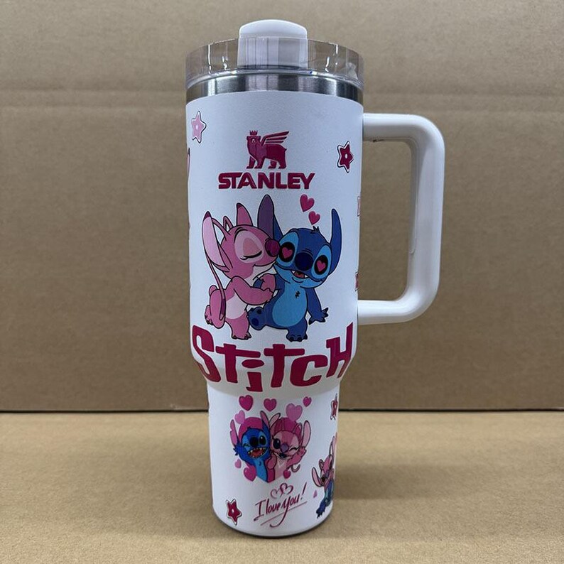 May include: A white Stanley tumbler with a handle and clear lid featuring a graphic of Stitch and Angel characters in blue and pink. The design includes red hearts, small stars, the text Stitch in large red letters, and the phrase I love you.