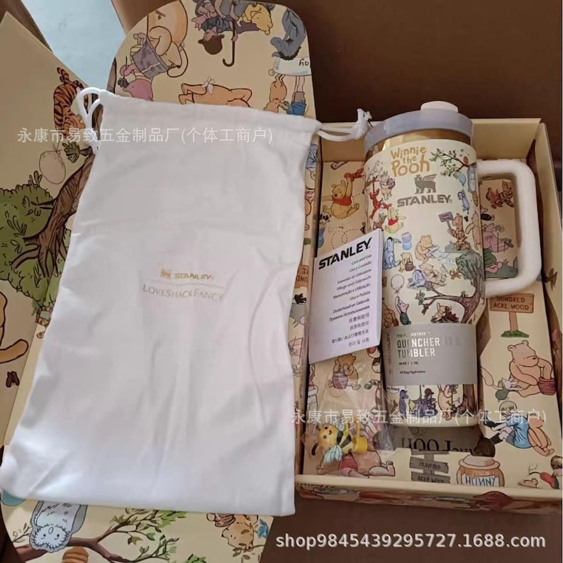 May include: A Stanley Winnie the Pooh Quencher tumbler with a handle, inside a decorative box. The tumbler features illustrations of Winnie the Pooh characters. A white drawstring bag and a tag are also in the box.