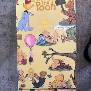 May include: A yellow box featuring illustrations of Winnie the Pooh characters. The box has the words "Winnie the Pooh" in large letters. Various characters are depicted, including Pooh, Eeyore, Piglet, and Tigger. The box also has the Stanley logo.