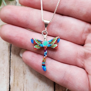 May include: A dragonfly pendant necklace featuring a mosaic inlay of multicolored stones including blue, green, red, and white segments. The dragonfly body and wings are set in silver, with a central circular stone and a delicate silver chain.