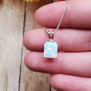 May include: A rectangular opal pendant necklace with a silver chain. The opal has a white base with flashes of blue, green, and yellow. The pendant is held in a silver setting. The chain is a delicate box chain.