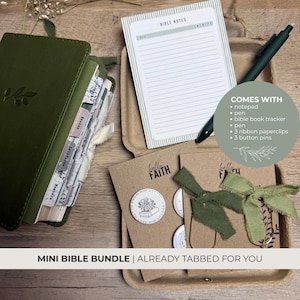 May include: A dark olive green Bible with tabbed pages, a lined notepad with the text BIBLE NOTES, a dark green pen, and two brown cards featuring round white button pins and green ribbon paperclips, all presented in a cardboard tray.