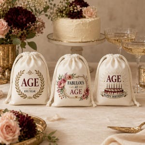 May include: Three off-white drawstring canvas favour bags featuring printed designs. The left bag shows a laurel wreath with the text AGE and EST. YEAR. The centre bag features a floral frame with the text FABULOUS AT AGE. The right bag displays a birthday cake with candles and the text AGE HAPPY BIRTHDAY.