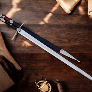 May include: A long, silver sword with a black handle and a silver crossguard, resting on a wooden surface. The sword is partially sheathed in a black scabbard with silver accents. Other items, including a compass and aged paper, are also on the wooden surface.