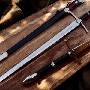 May include: Three swords with sheaths on a wooden surface. The swords have silver blades and black handles. One sword has a black sheath with silver accents, and another has a gold hilt.