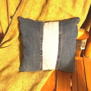 Pu&ograve; includere: Un cuscino di jeans con una striscia bianca al centro. Il cuscino &egrave; su una coperta gialla.