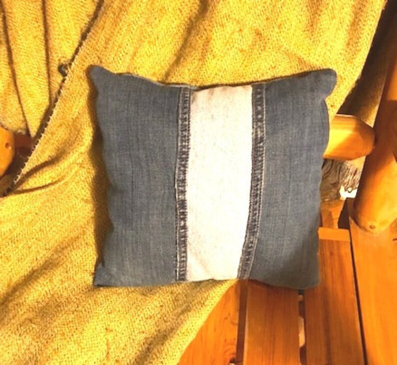 Pu&ograve; includere: Un cuscino di jeans con una striscia bianca al centro. Il cuscino &egrave; su una coperta gialla.