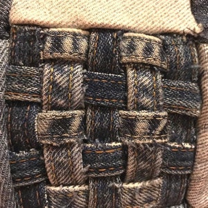 Pu&ograve; includere: Primo piano di un tessuto intrecciato realizzato con strisce di denim in tonalit&agrave; di blu e marrone. Il tessuto &egrave; intrecciato a forma di cesto.