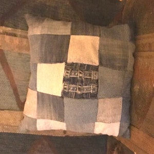 Pu&ograve; includere: Un cuscino quadrato a patchwork realizzato in tessuto denim in tonalit&agrave; di blu e bianco. Il cuscino ha un design in denim intrecciato al centro.