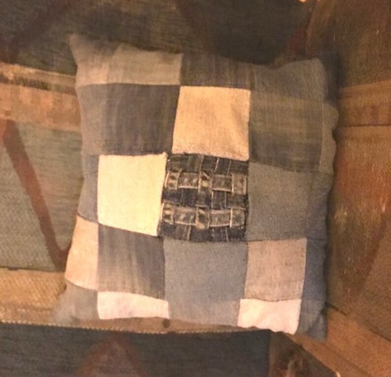 Pu&ograve; includere: Un cuscino quadrato a patchwork realizzato in tessuto denim in tonalit&agrave; di blu e bianco. Il cuscino ha un design in denim intrecciato al centro.