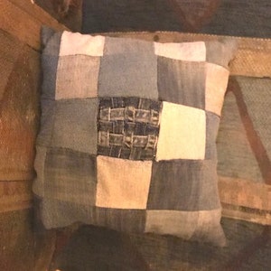Pu&ograve; includere: Un cuscino quadrato a patchwork realizzato in tessuto denim in tonalit&agrave; di blu e bianco. Il cuscino ha un motivo a scacchi con un quadrato centrale in denim intrecciato.