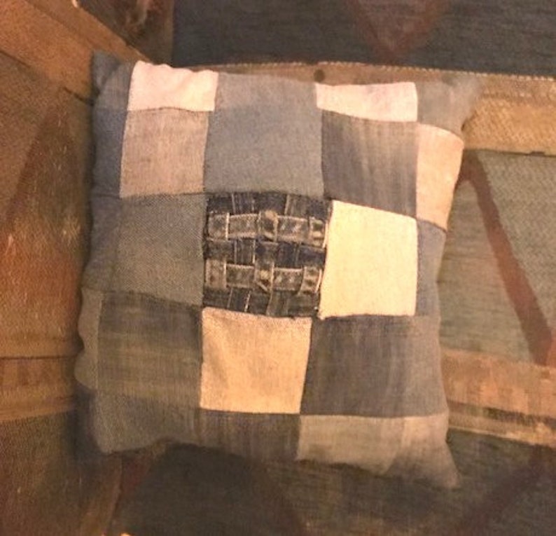Pu&ograve; includere: Un cuscino quadrato a patchwork realizzato in tessuto denim in tonalit&agrave; di blu e bianco. Il cuscino ha un motivo a scacchi con un quadrato centrale in denim intrecciato.