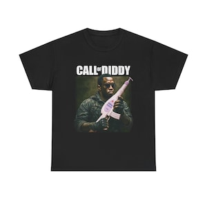 May include: Black t-shirt featuring the text "CALL OF DIDDY" above an image of a person holding a baby lotion bottle modified to look like a weapon. The person is wearing sunglasses and gloves. The shirt is a casual wear item.