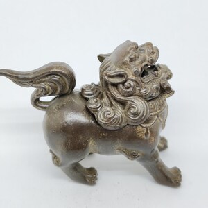 May include: A bronze-coloured, detailed figurine of a mythical lion-like creature. The sculpture features intricate details, including flowing mane, curled tail, and a fierce expression. The figurine is posed in a walking stance, showcasing its four legs.