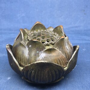 May include: A bronze-coloured lotus flower-shaped incense burner. The burner has detailed petal designs and a perforated top. The overall aesthetic is antique and decorative, suitable for spiritual or home decor.