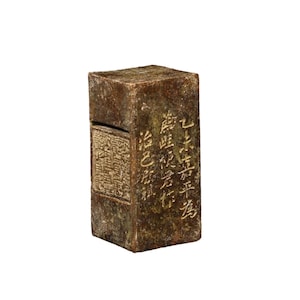 May include: A rectangular, antique-looking, brown stone seal with carved Chinese characters. The seal has a rectangular recessed area with more detailed carvings. The stone has a weathered appearance.