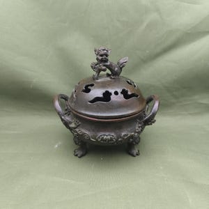 以下が含まれることがあります： 雲の形をした切り抜きと、上部に神話上の生き物の小さな像が付いた蓋が付いたブロンズの香炉。バーナーには2つのハンドルがあり、3つの脚の上に置かれています。 全体的なデザインは装飾的で詳細です。