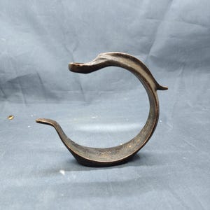 May include: A bronze-colored, curved metal object with a circular design. The object has a smooth, polished finish and a unique, artistic shape. The design features a small, raised platform at the top and a curved base.