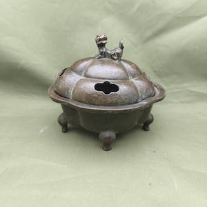 以下が含まれることがあります： 小さな動物のフィギュアが付いた蓋が付いた、ブロンズ色の香炉。バーナーは、3つの小さな足で支えられた丸いベースを持っています。蓋は、いくつかの開口部を備えた装飾的な形状をしています。