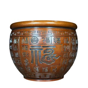 May include: A round, wooden decorative bowl with a wide rim. The bowl is carved with Chinese characters and cloud designs. The bowl is a warm brown color and has a smooth finish. The bowl is likely used for decorative purposes.