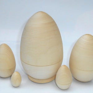 Puede incluir: Un conjunto de muñecas rusas de madera sin terminar, con forma de huevo. La más grande mide unos 20 cm de alto, la más pequeña unos 5 cm. La veta natural de la madera es visible en cada huevo. Listas para pintar o decorar.