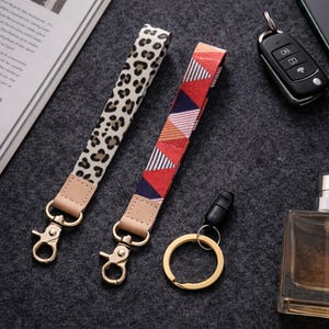 May include: Two keychains with gold-tone clasps and leather accents. One has a leopard print, the other a geometric pattern in red, blue, and orange. A gold key ring and car key are also visible.