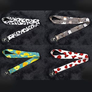 Puede incluir: Cuatro cordones con diseños y cierres metálicos se muestran sobre un fondo oscuro. Los diseños incluyen caras de panda sobre blanco, gatos sobre gris, pollitos amarillos sobre turquesa y mariquitas rojas sobre blanco. Cada cordón está doblado en zigzag.