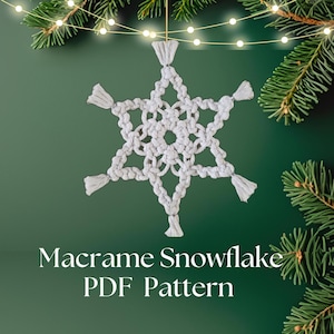 Puede incluir: Un adorno de copo de nieve de macramé blanco con un diseño de estrella de seis puntas, colgado sobre un fondo verde con ramas de pino y luces de cadena. El texto "Macrame Snowflake PDF Pattern" está debajo.