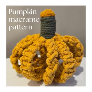 Pode incluir: Uma abóbora de macramé feita à mão em tons de amarelo, verde e laranja. A abóbora é feita de fio grosso e trançado, com um caule e detalhes na parte superior. O texto "Pumpkin macrame pattern" é exibido em branco.