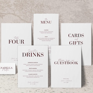 Puede incluir: Un conjunto de papelería de boda blanca con texto burdeos. El conjunto incluye un menú, un número de mesa, un letrero de libro de visitas y un letrero de tarjetas y regalos. El menú enumera las opciones de entrantes y plato principal.
