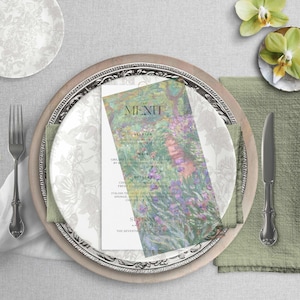 Puede incluir: Una mesa formal con una tarjeta de menú floral, un plato decorativo, un tenedor, un cuchillo y una servilleta verde. La tarjeta del menú presenta una colorida escena de jardín. El plato tiene un diseño floral.