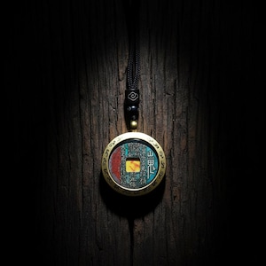 May include: A round pendant necklace with a coin-like design. The pendant has a gold-colored frame and a central design with red, yellow, and blue hues. The necklace has a black cord.