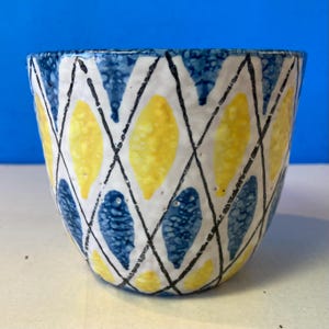 May include: A ceramic bowl with a distinctive pattern. The bowl has a white base adorned with yellow and blue leaf-shaped motifs, outlined in black. The rim is blue. This bowl is likely intended for serving or decorative purposes.