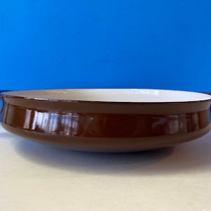 May include: A brown enamelled cast iron pan with two handles. The pan has a white interior.