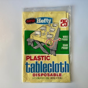 Puede incluir: Un mantel de plástico amarillo con las palabras "new Hefty" y "PLASTIC tablecloth DISPOSABLE" impresas en él. El mantel mide 101,6 cm x 198,1 cm (101,6 cm x 198,1 cm). Se anuncia como a prueba de viento, a prueba de remojo y se limpia con un paño. El precio es de 25 centavos.