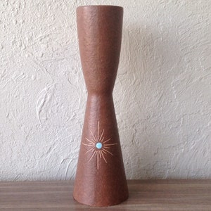 Puede incluir: Un portavelas de cerámica marrón con un diseño de estrella y un centro azul claro. El portavelas tiene una superficie texturizada.