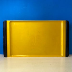 May include: A rectangular yellow serving tray with black accents on the short ends. The tray has a glossy finish and is set against a blue background. The tray is designed for serving food and drinks.