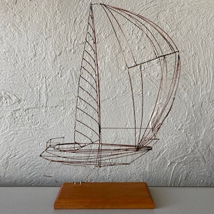 May include: A wire sculpture of a sailboat with a wooden base. The sailboat is made of thin, brown wire and has a detailed design. The base is a rectangular piece of wood.