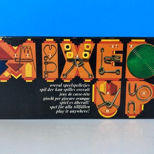 May include: A black box with the word "MIXED UP" in colorful, geometric letters. The box features various metal puzzles and the text "play it anywhere!"