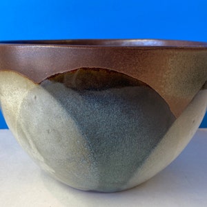 May include: A ceramic bowl with a unique color gradient. The rim is a dark brown, transitioning to shades of gray, blue, and white on the exterior. The bowl has a smooth, rounded shape, suitable for serving or display.